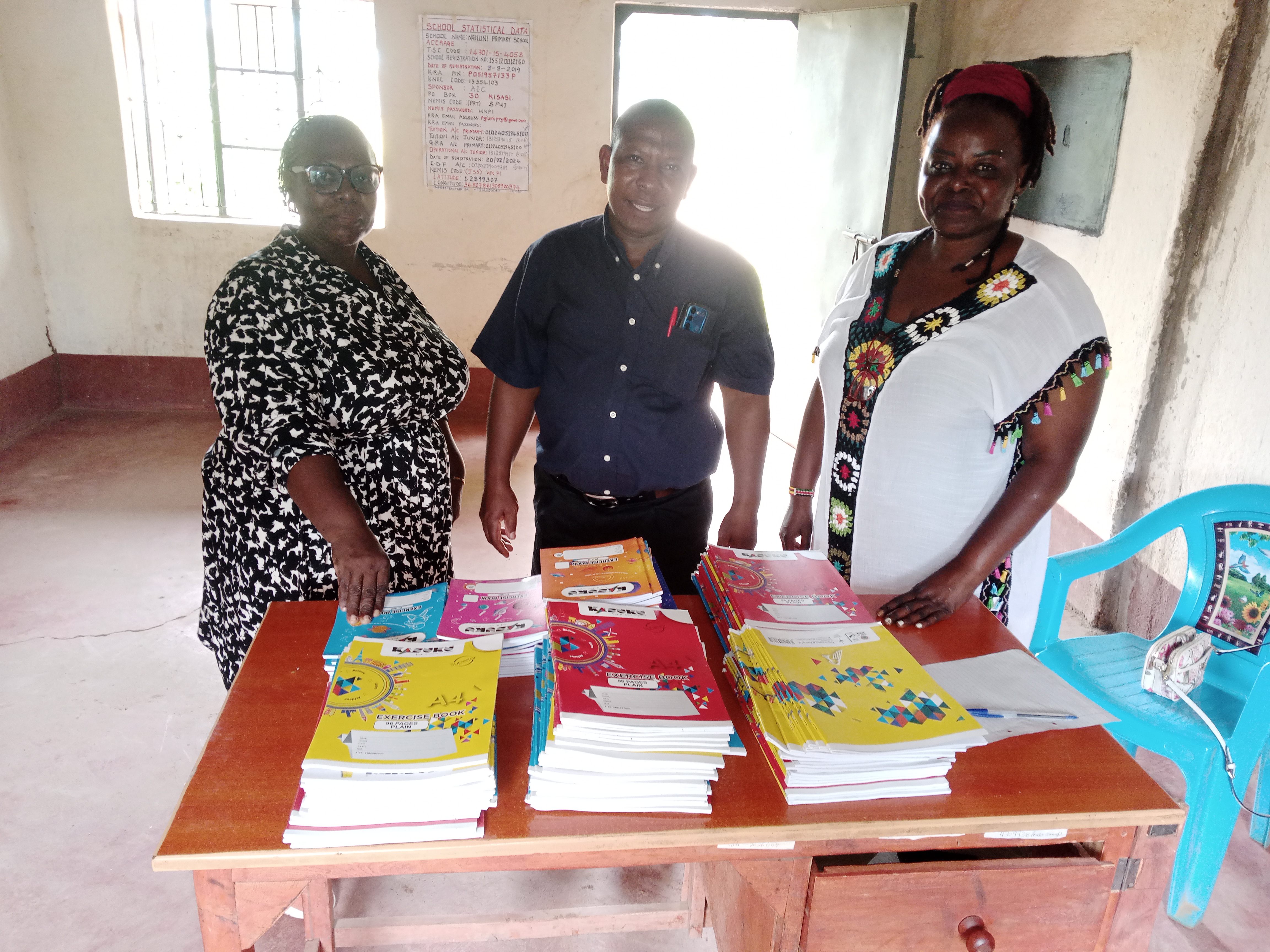 Official handing over the exercise books to the School Headteacher, Mr Joseph. 